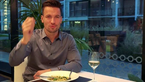 A young, handsome man sits at a table in a restaurant and calls a waiter Stock Footage 72153581
