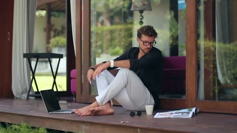 Young handsome man is sitting and using a smartphone outside the house. Stock-Footage 85524747