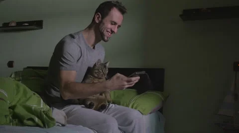 Young handsome man sitting on the bed and taking a selfie with the cat Stock Footage 59842831