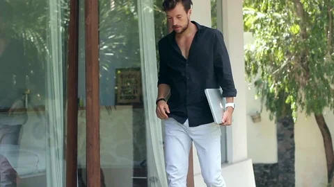 Young handsome man is sitting down on the terrace and using a laptop outside the Vidéo 85525011