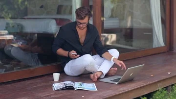 Young handsome man is sitting down on the terrace, talking on the phone and Stock-Footage 85525138