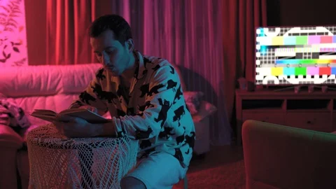 A young, handsome man is sitting at a table reading a book Stock Footage 128458039