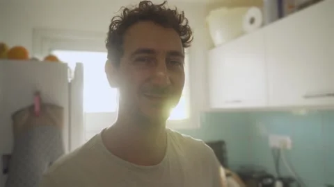 Young handsome man smiling to camera stands in small apartment kitchen backlight Stock Footage 131900533