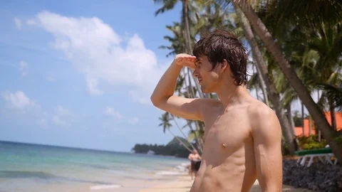 Young handsome man standing on the beach enjoying sunny day on his vacation Video stock 88137679