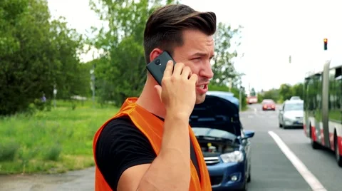 Young handsome man stands in front of car dressed in reflective vest and phones  Video stock 67749310