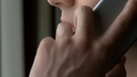 A young handsome man in a suit talking on a mobile phone near a large window Stock Footage 77195527