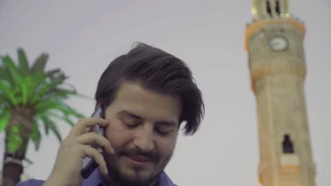 Young handsome man talking to phone front of clock tower in the center of Izmir  Vídeos de archivo 77066896