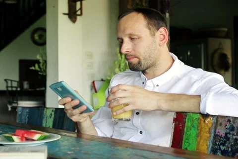 Young, handsome man texting on smartphone sitting by table at home NTSC Stock Footage 39514044