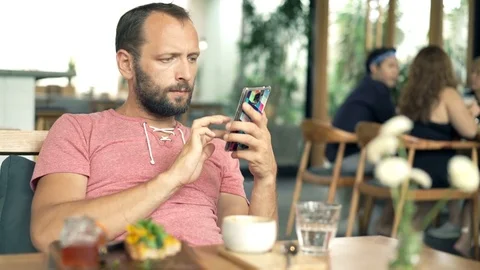 Young, handsome man texting on smartphone and drinking beverage in cafe, 4K Stock Footage 70790797