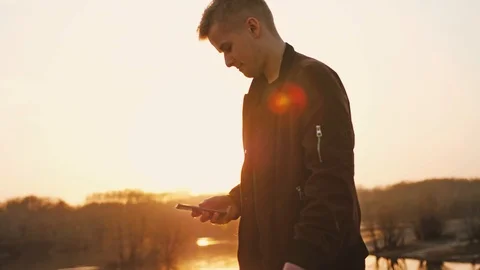 Young handsome man uses smart phone walks at beautiful sunset on the beach. slow Stock Footage 108721177