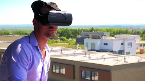Young handsome man uses virtual reality glasses on the balcony - buildings and Vídeo Stock 79049875