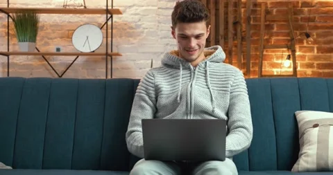 Young Handsome Man using his Laptop at Home, having cute Smile. Man is chatting Stock Footage 130353269