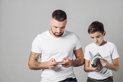 Young handsome man using his smart phone while his little brother holding a book Stock Photos