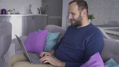 Young, handsome man using laptop sitting on sofa Stock Footage 74730723
