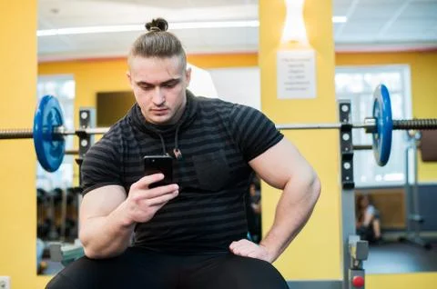 Young handsome man using phone while having exercise break in gym Stock Photos
