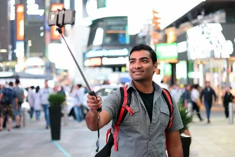 Young handsome man using selfie stick in busy urban city Stock Photos