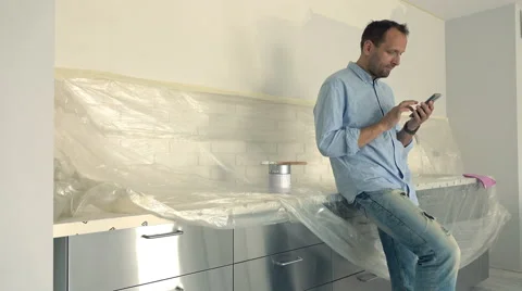 Young, handsome man using smartphone during renovation his new home, 4K Stock Footage 64550217