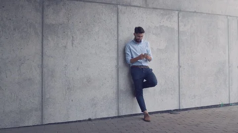 Young handsome man using smartphone while leaning against wall Stock Footage 112868908