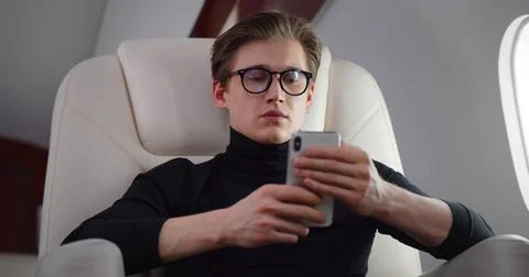 Young handsome man using smartphone flying business class Stock Photos