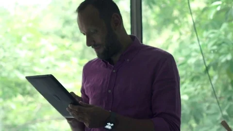 Young, handsome man using tablet computer by window at home Stock Footage 76950239