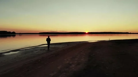 A young handsome man is walking on an empty beach at sunset. a shadow Video stock 160069910