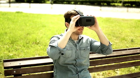 Young handsome man wearing virtual reality goggles sitting on the bench Stock Footage 64919699