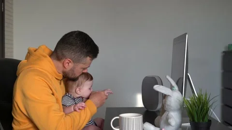 Young handsome man working on a desktop computer at home with a baby in his arms Stock Footage 151036059