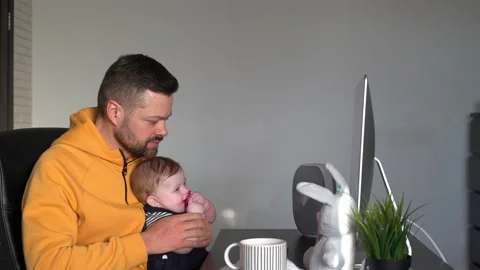 Young handsome man working on a desktop computer at home with a baby in his arms Stock Footage 151036190