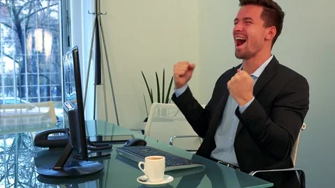 A young, handsome man works on a computer in an office and starts to celebrate Stock-Footage 71997371