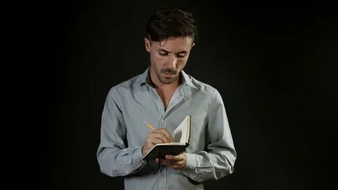 Young handsome man writing on notepad on neutral black background Stock Footage 80303616