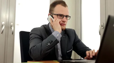 Young, handsome men sitting behind the desk and talking thru the phone Stock Footage 49339879