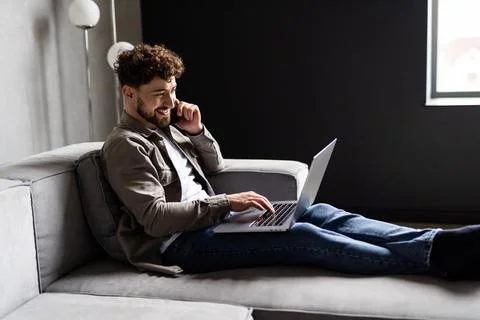 Young handsome millennial man sitting on couch in living room at home using c Stock Photos