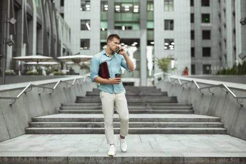 Young handsome office worker talking on phone holding laptop and cup of coffee Foto stock