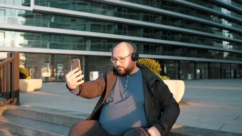 Young handsome plus size man wearing wireless headphones taking selfie by his Video stock 232577642