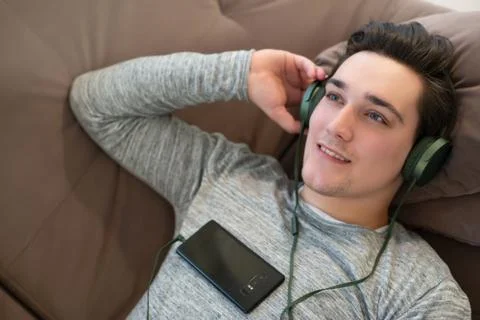 Young handsome relaxed man lying on the sofa listening to music in earphones Stock Photos