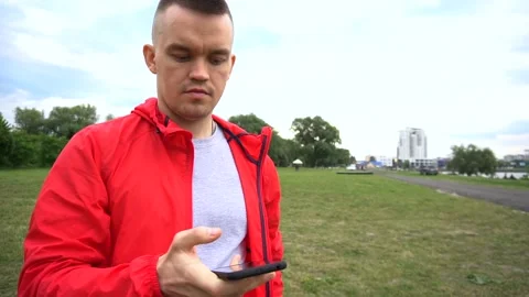 Young handsome runner in red hook wear surfes internet on cellphone Video stock 90844127