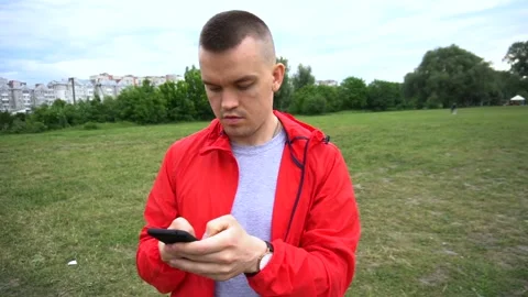 Young handsome runner in red hook wear surfes internet on cellphone Stock Footage 90844412