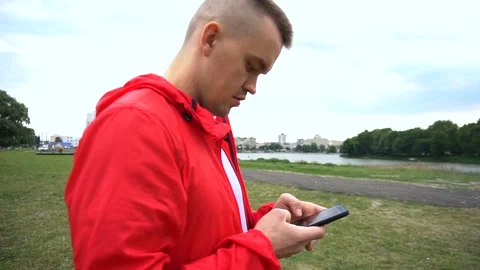 Young handsome runner in red hook wear surfes internet on cellphone Stock Footage 90845984