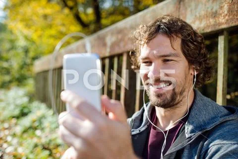 Young handsome runner with smart phone sitting on a bridge Stock Photos