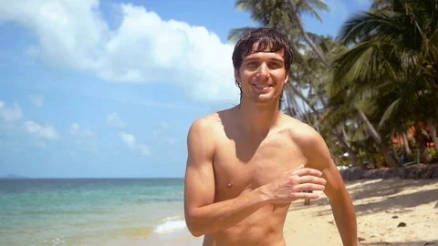 Young handsome smiling man running on the beach to the camera at sunny day. slow Stock Footage 87946900