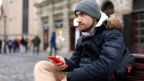 Young handsome stylish man using red smartphone outside smiling cheerful looking 스톡 동영상 121308846