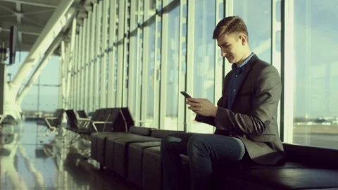 Young handsome is thumbng a text message while sitting in airport Stock Footage 77637771