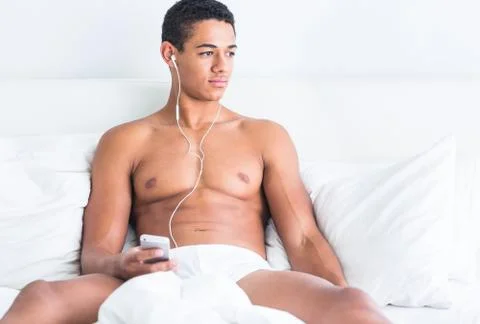 Young handsome topless black man enjoying music in bed. Stock Photos