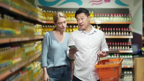 Young happy Asian couple using smartphone in supermarket with shopping cart  Stock Footage 199845620