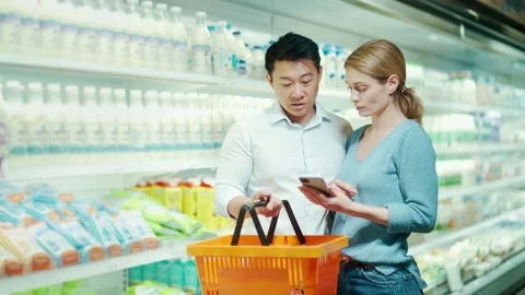 Young happy Asian couple using smartphone standing in supermarket with shopping  Stock Footage 199846387