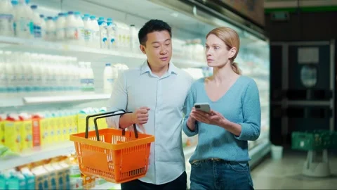Young happy Asian couple using smartphone in supermarket with shopping cart  Stock Footage 199846497