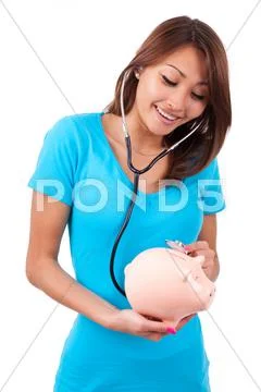 Young happy beautiful asian woman using stethoscope on her piggy bank - asian Stock Photos