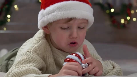 Young happy boy lying on bed during cozy winter evening, exploring red white Stock Footage 322195778