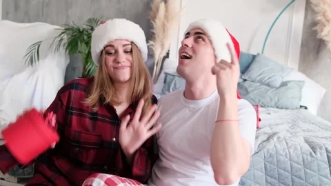 Young happy couple dancing and dabbles on the floor near bed wearing santa hats 스톡 동영상 144957915