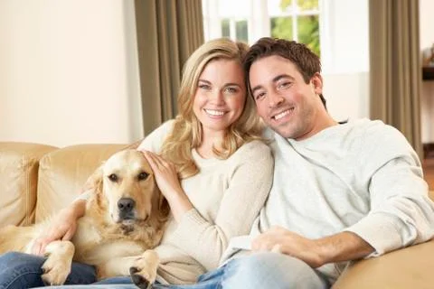 Young happy couple with dog sitting on sofa Stock Photos
